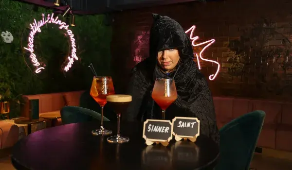 Woman in black cloak with drinks in front on a table