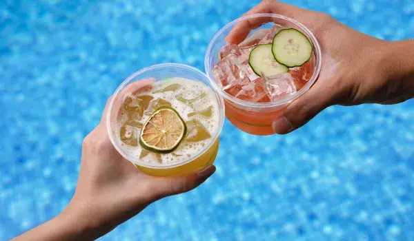 Two hands with cocktails held over a swimming pool