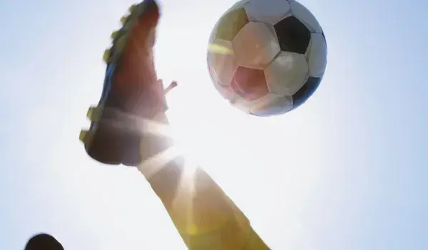 A man kicking a football into the sun