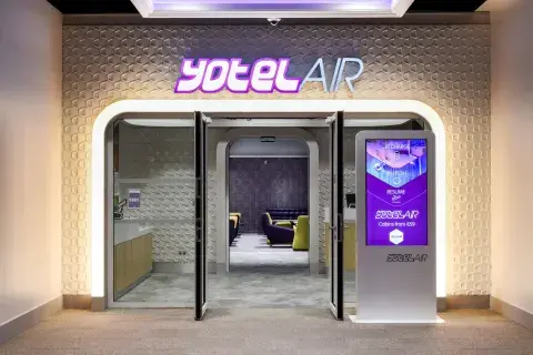 Entrance lobby to an airport hotel with digital display screen, a check-in desk and glowing YOTELAIR lettering 