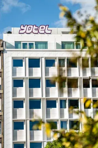 Blue sky and green trees overlooking the white facade of YOTEL Porto