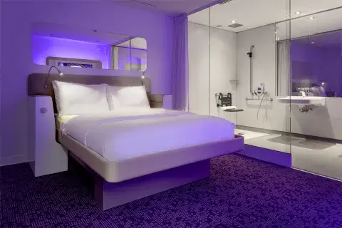 A large purple hotel room with mood lighting, a bright ensuite bathroom and mirror