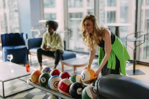 A girl lifts a bowling ball in a top-floor bar while her friend looks on
