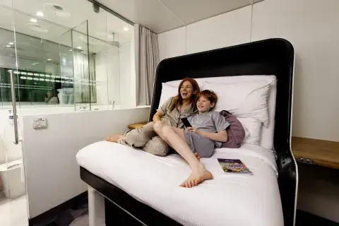 A mother and her son lie back in bed laughing, watching a show on TV