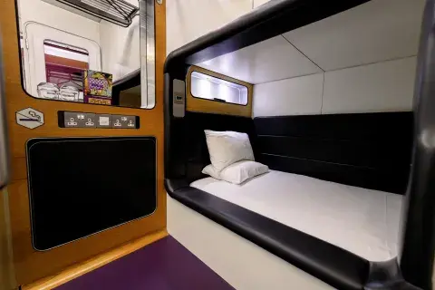 A hotel room with a single bed, a charging station, mirror, and purple carpet