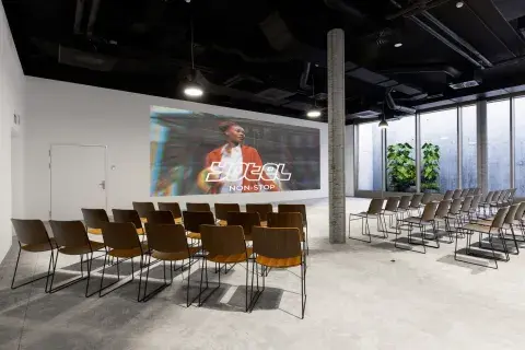 A large meeting room with a huge flatscreen tv, bright windows and plants