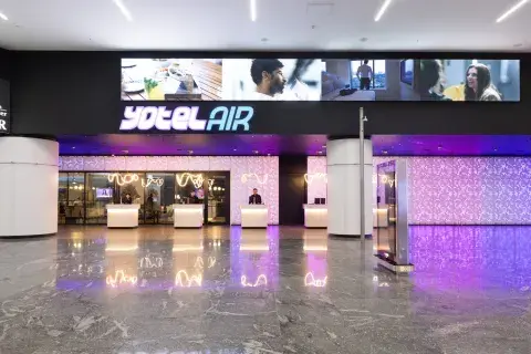 A large hotel facade inside the airport with 5 check-in kiosks. Above there are dynamic screens and the title YOTELAIR