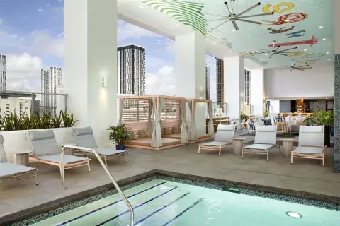 A large outdoor pool positioned high up in a city, featuring lounge chairs, a painted ceiling and cabanas