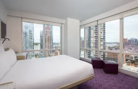 Brightly lit hotel room with floor-to-ceiling windows looking out towards the New York skyline