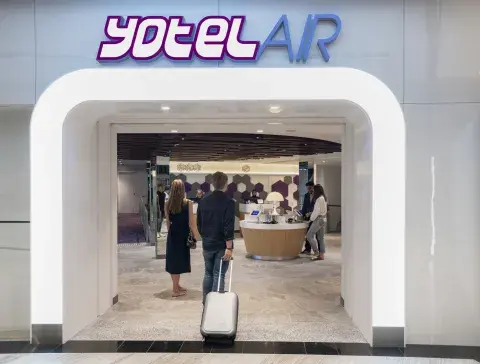 People with suitcases walk into an airport hotel entrance, the sign above reads YOTELAIR