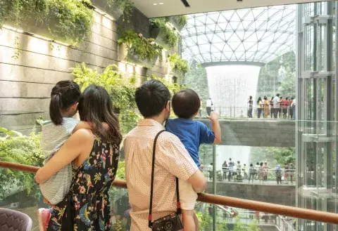 A family stand on the mezzanine balcony of Singapore Changi Airport and admire the indoor rain vortex. Wow!