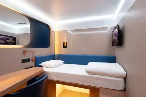 A compact, smart hotel room with a single bed, desk, mirror, TV and luggage storage space