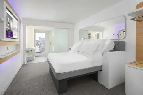 A large well-lit hotel room with a big bed, TV screen, bathroom and floor-to-ceiling windows