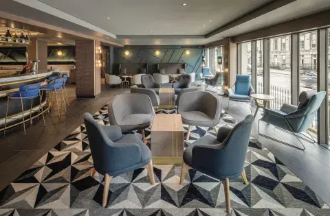 A hotel bar and restaurant with patterned carpet, blue chairs and a round bar