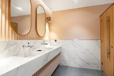 A modern bathroom with two oval mirrors and marble counter tops 