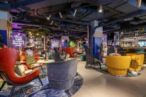 A colourful and rustic bar and restaurant with red and yellow seats and a factory-style ceiling