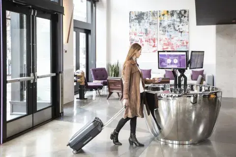 A woman uses a self-service check-in machine at a hotel lobby with her luggage, 