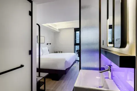 A large Queen Sized Room at YOTEL Tokyo with bright windows and a compact bathroom